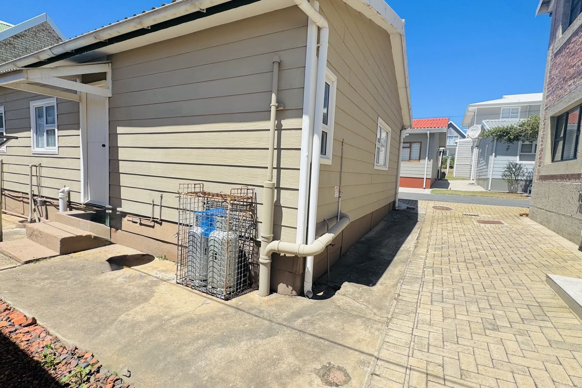 Side exterior view of the property featuring weatherboard cladding, paved walkway, and a secured gas cylinder storage area.