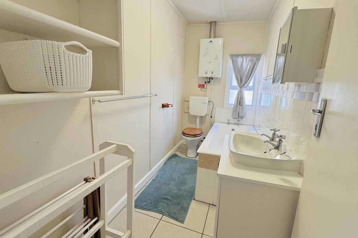 A functional bathroom featuring a bathtub, pedestal basin, toilet, and wall-mounted gas geyser, with built-in shelving for storage.