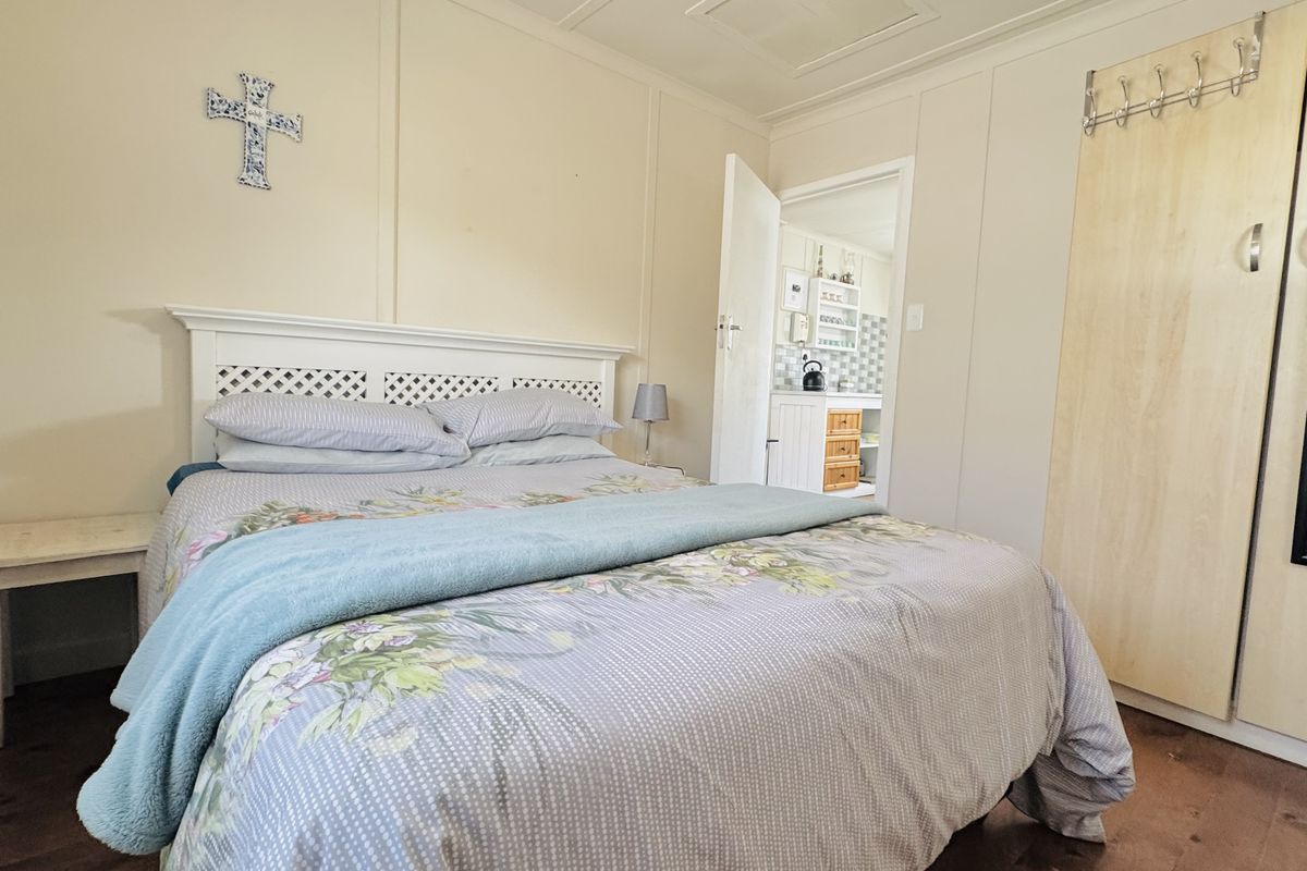 A bedroom featuring built-in wooden cabinetry and a view into an adjacent kitchen area with tiled splashback.