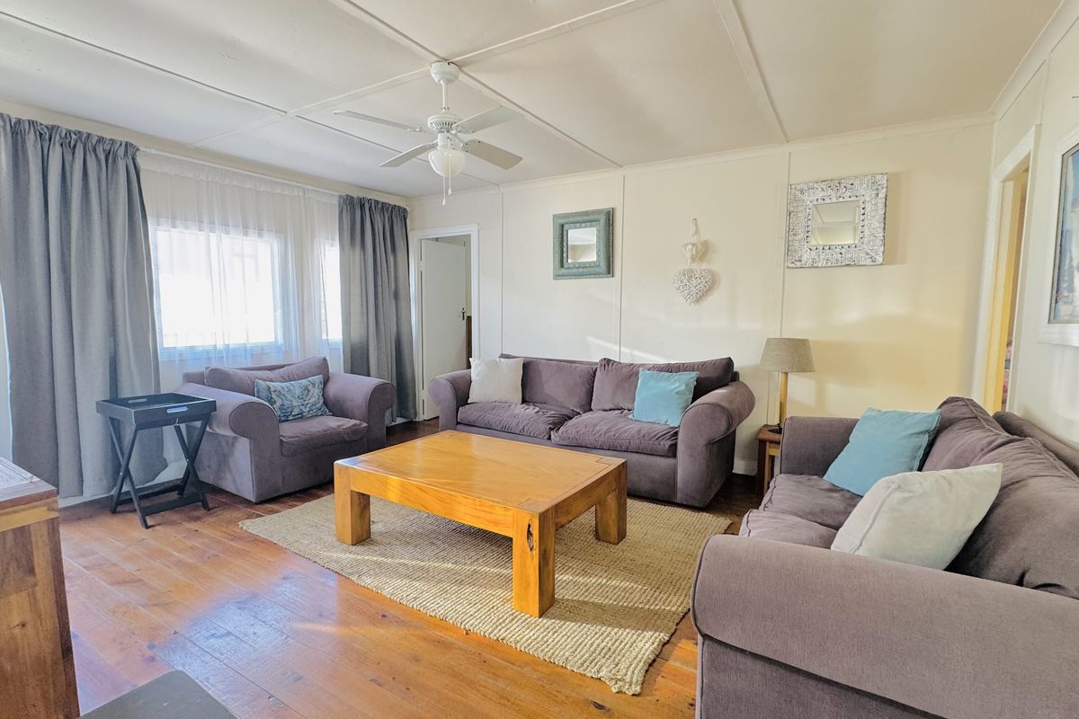 A comfortable living room featuring timber flooring, a ceiling fan, and large windows that allow for natural light.
