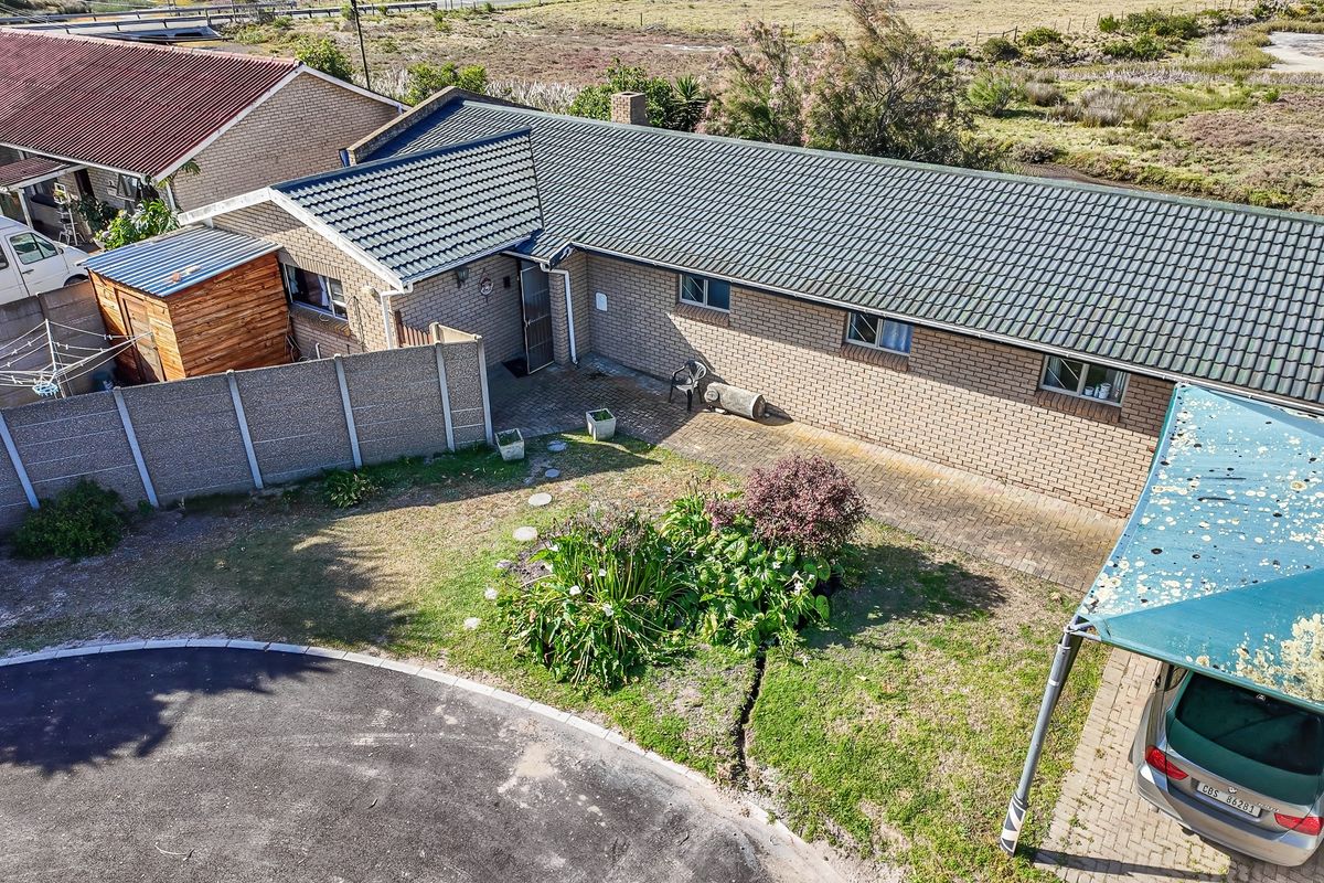 Aerial view of a brick house featuring a tiled roof, paved courtyard area, and a small garden with a shaded parking structure.