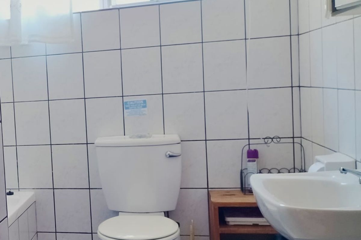 A functional bathroom featuring white wall tiles, a pedestal basin, and a standard toilet with a window for natural light.