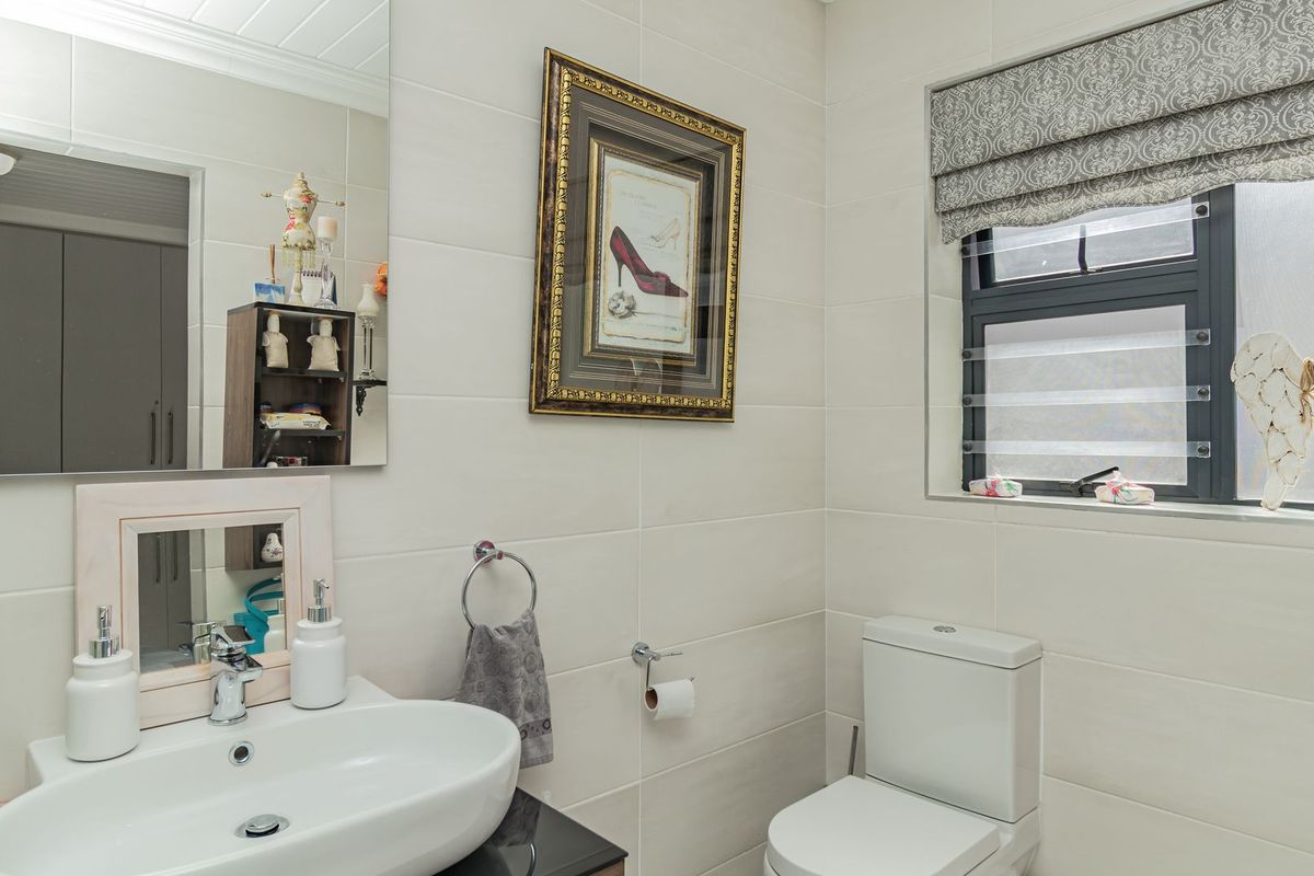 A well-maintained bathroom featuring a wall-mounted basin, modern toilet, tiled walls, and a window with a roman blind.