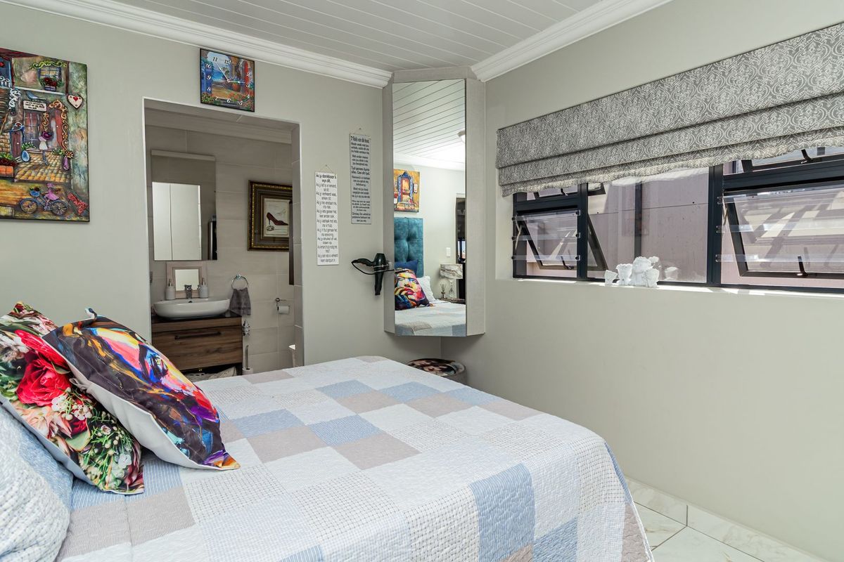 A well-maintained bedroom featuring tiled flooring, corner mirror, and an adjoining en-suite bathroom with a modern vanity basin.