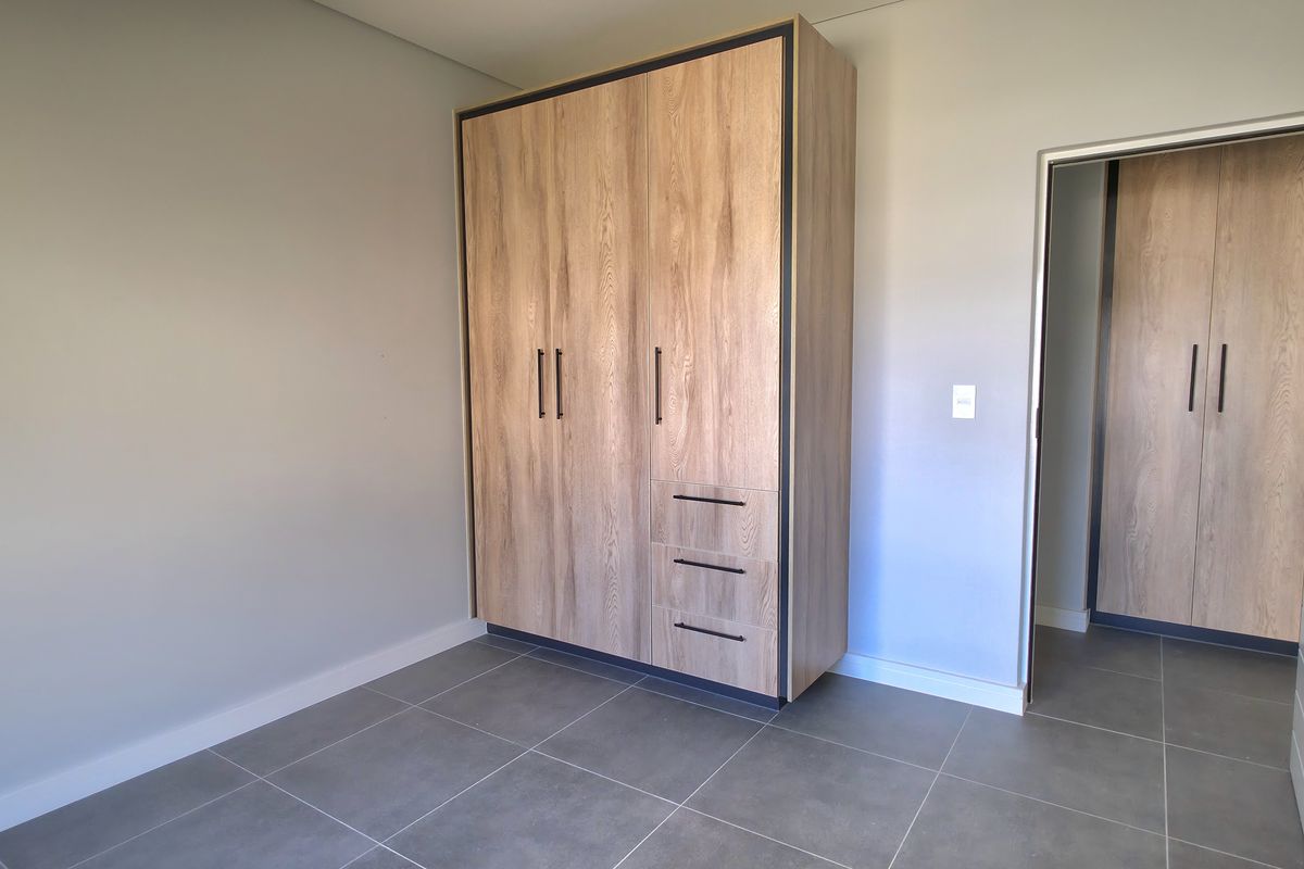 A bedroom featuring modern wood-grain built-in cupboards, neutral wall finishes, and large format grey floor tiles.