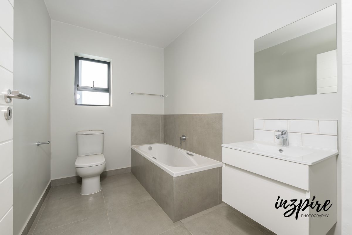 A clean, modern bathroom featuring a built-in bathtub, a wall-mounted vanity with a basin, and a toilet, finished with neutral grey floor and wall tiles.