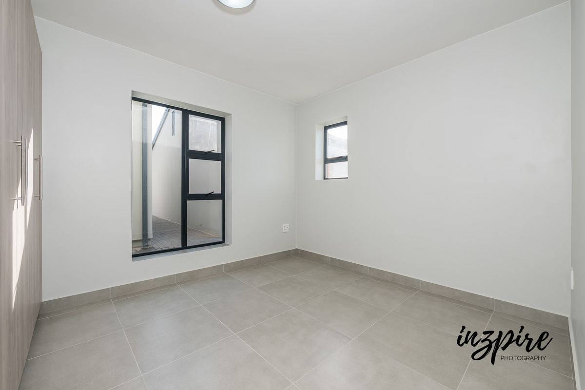 A bright, empty bedroom featuring neutral floor tiles, built-in cupboards, and modern black-framed windows.
