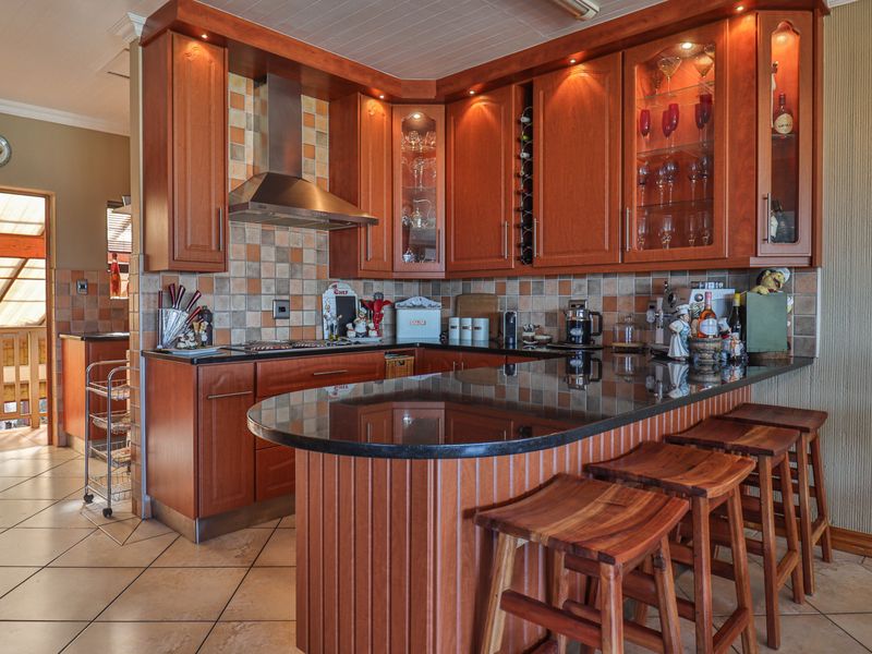 A well-maintained kitchen featuring warm wooden cabinetry, granite countertops, a breakfast bar, and a tiled backsplash with integrated hob and extractor fan.