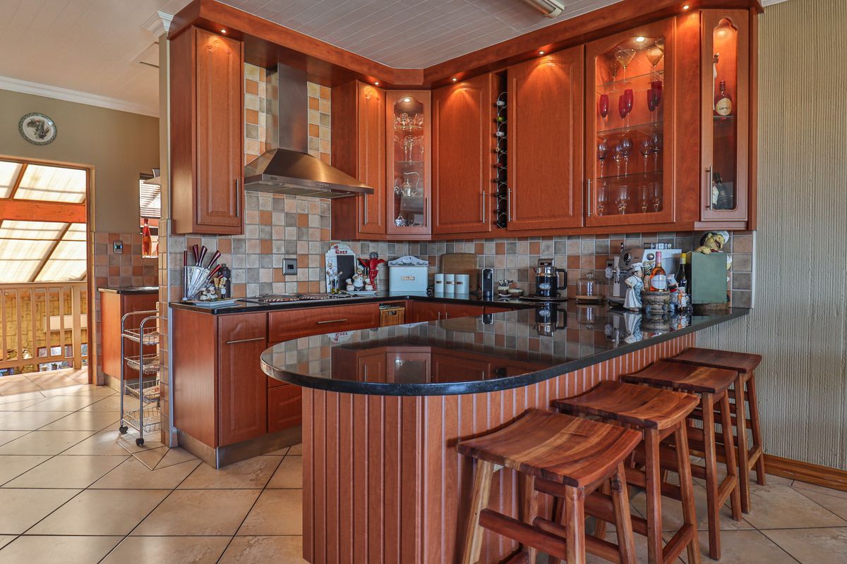 A well-maintained kitchen featuring warm wooden cabinetry, granite countertops, a breakfast bar, and a tiled backsplash with integrated hob and extractor fan.