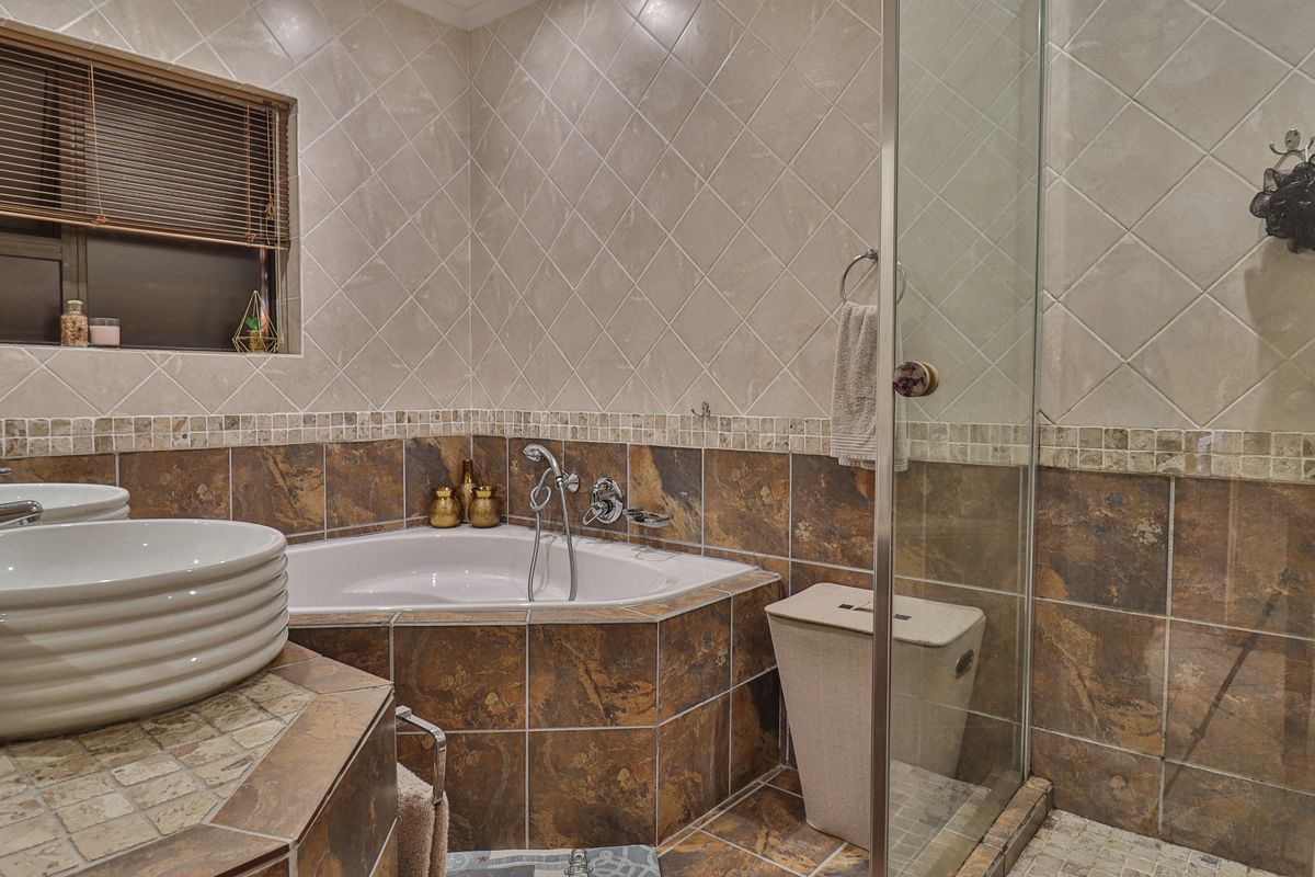 A bathroom featuring a corner bathtub, glass-enclosed shower, and a tiled vanity with a vessel sink, finished with decorative mosaic tile accents.