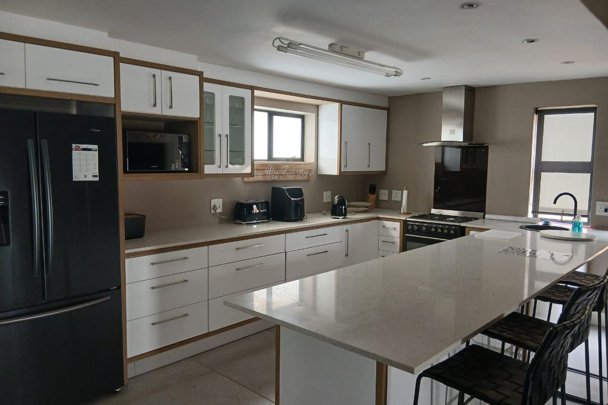 Modern kitchen featuring white cabinetry, stone countertops, a central island with breakfast bar seating, and stainless steel built-in appliances.