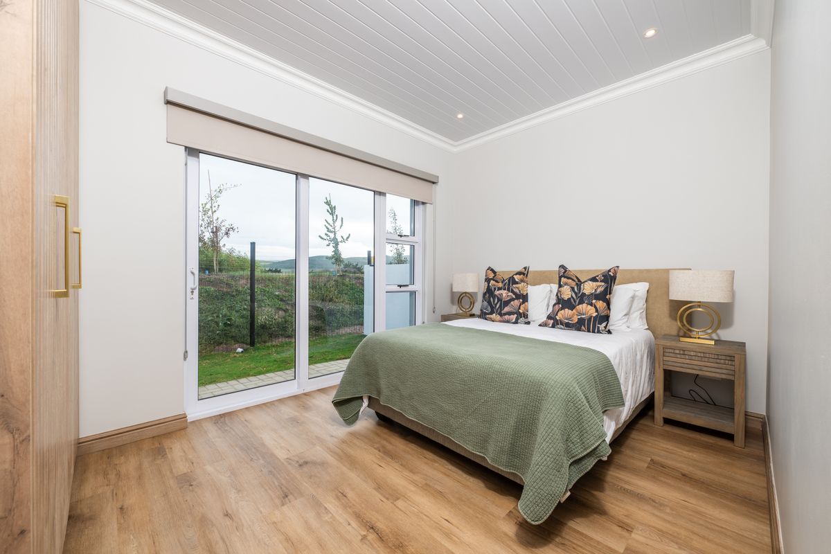 A bright bedroom featuring wood-look flooring, built-in cabinetry, and large sliding glass doors that provide direct access to the garden.
