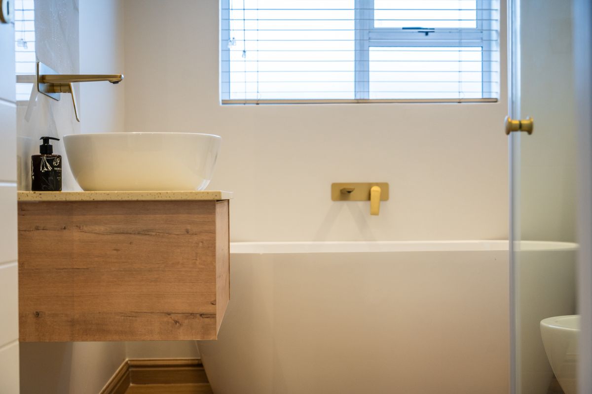 Modern bathroom featuring a wall-mounted wooden vanity, vessel sink, freestanding bathtub, and contemporary gold-toned fixtures.