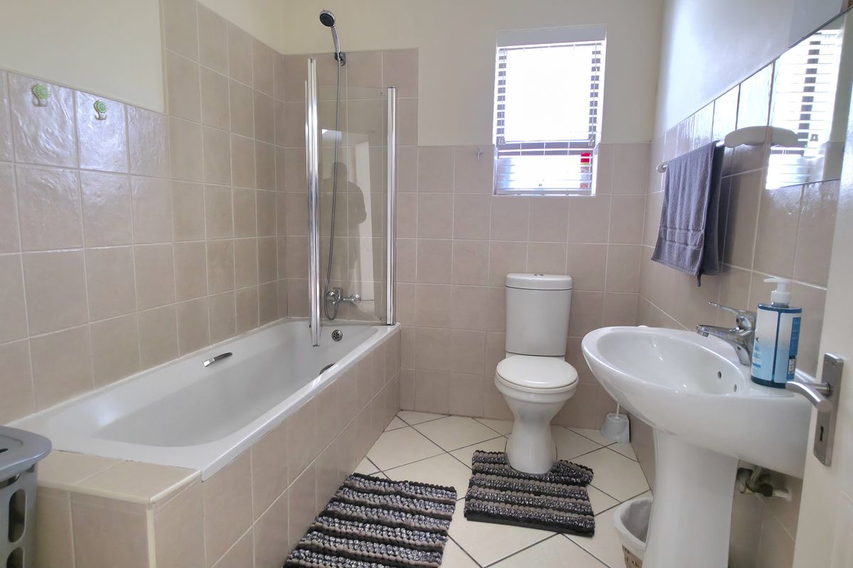 A functional bathroom featuring a bathtub with a glass shower screen, a pedestal basin, and a standard toilet with neutral wall and floor tiling.
