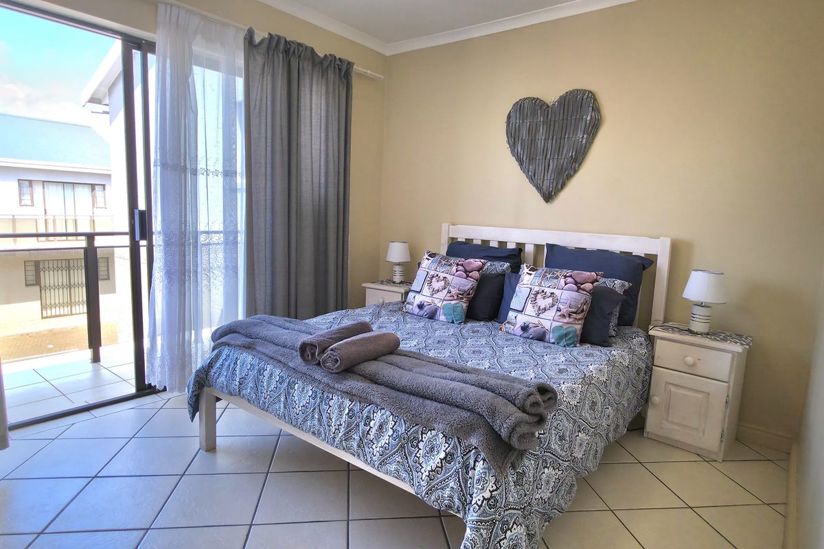 A bright bedroom featuring tiled flooring and sliding glass doors that open onto a private balcony, providing natural light and outdoor access.