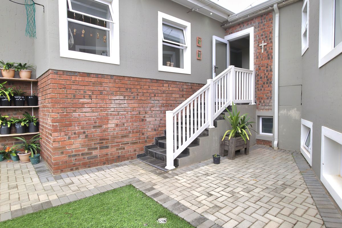 A rear exterior view featuring a paved courtyard, brick and rendered wall finishes, and a staircase leading to an elevated entrance.