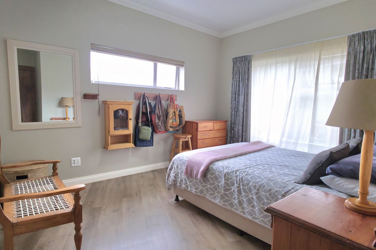 A well-maintained bedroom featuring light wood-look flooring, neutral wall tones, and large windows that provide ample natural light.