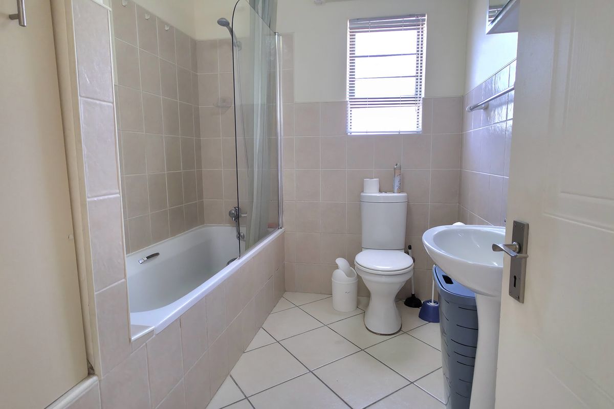 A functional bathroom featuring a bathtub with a glass shower screen, a pedestal basin, and a toilet, finished with neutral wall and floor tiles.