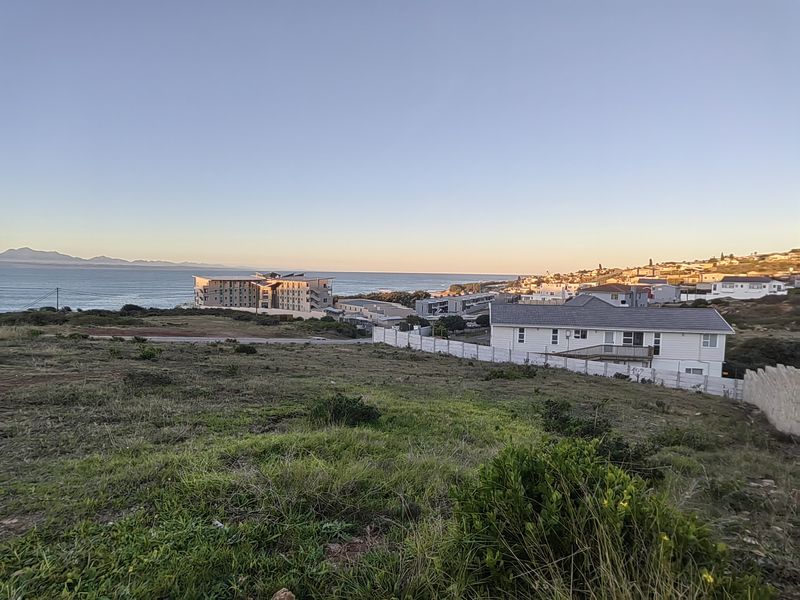 A scenic elevated view overlooking a coastal residential area with ocean vistas and distant mountain ranges.