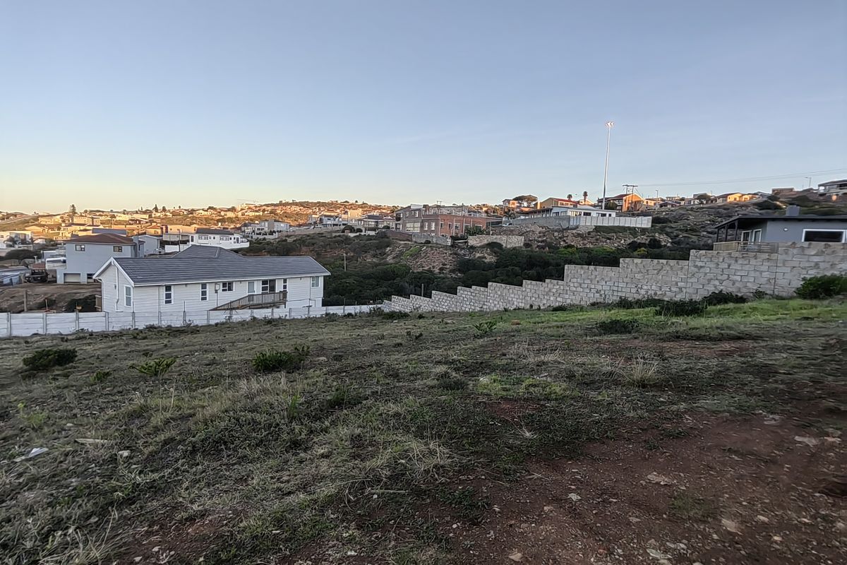 A view of the vacant residential land featuring a stepped concrete block retaining wall and surrounding neighborhood landscape.