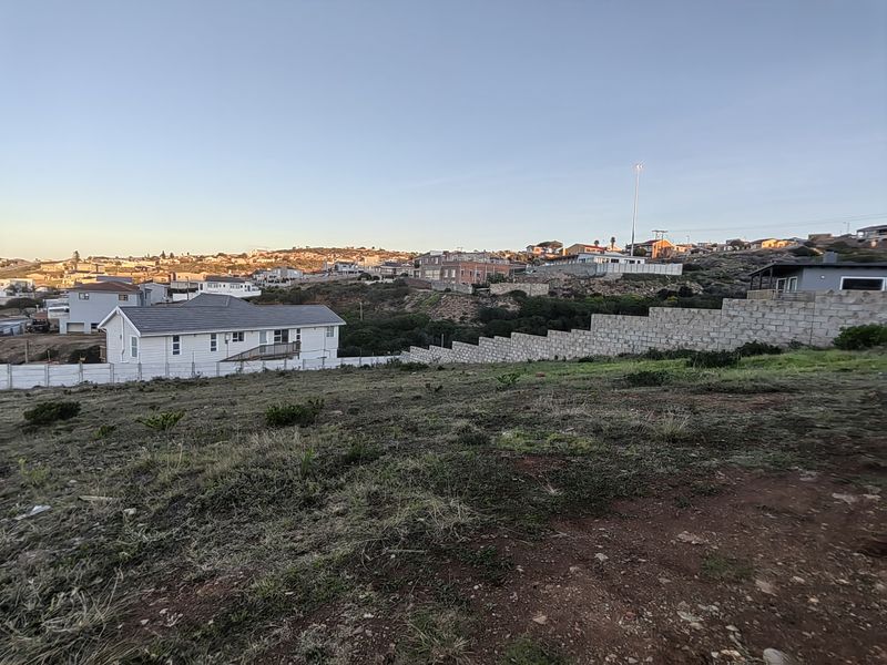 A view of the vacant residential land featuring a stepped concrete block retaining wall and surrounding neighborhood landscape.