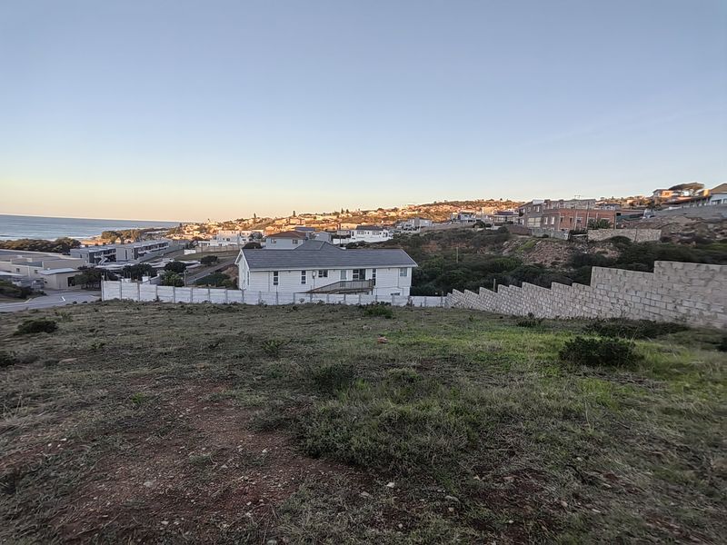 Elevated view overlooking a residential neighborhood and the coastline, featuring established boundary and retaining walls on the vacant land plot.