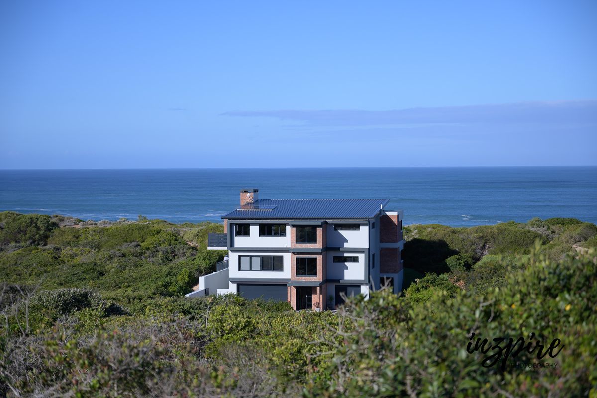 An elevated aerial view of a modern multi-story coastal home featuring brick and rendered finishes, a metal roof, and a double garage.