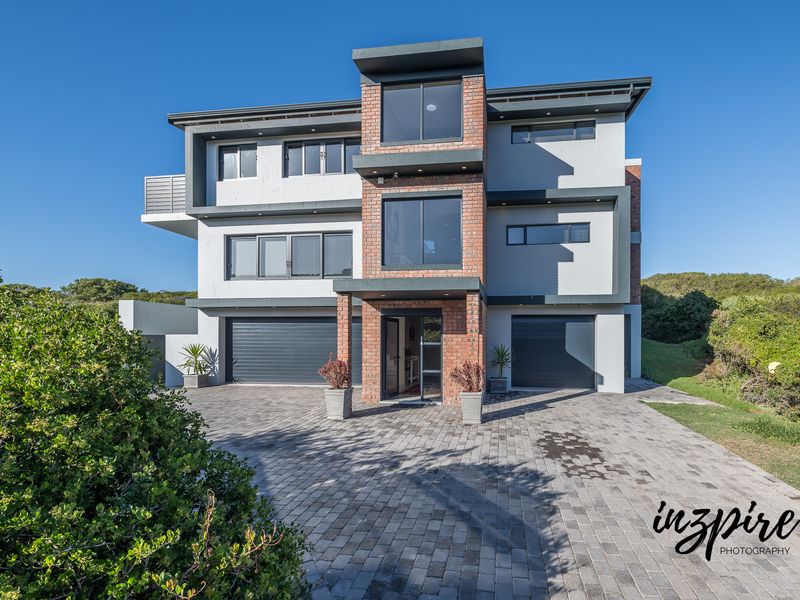 Modern three-story residential property featuring a brick and plaster facade, double garage, paved driveway, and contemporary aluminium window frames.