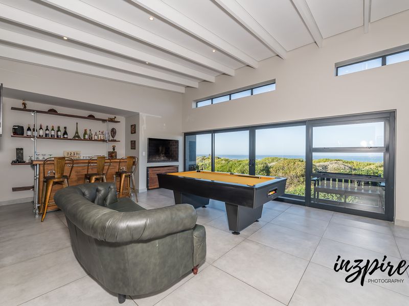 Spacious entertainment room featuring a built-in bar, exposed beam ceiling, fireplace, and large sliding doors offering scenic coastal views.