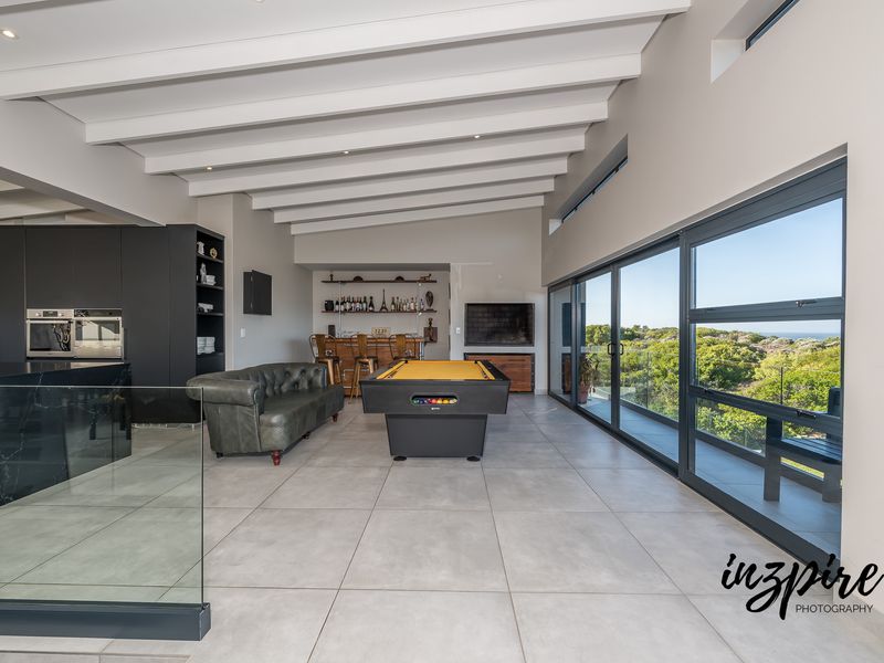 Spacious open-plan living area featuring exposed ceiling beams, modern kitchen cabinetry, a built-in bar, and large sliding doors opening to a scenic view.