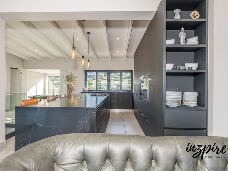 Modern kitchen featuring a large stone-topped island, integrated cabinetry, built-in oven, gas cooktop, and stylish exposed ceiling beams with recessed lighting.