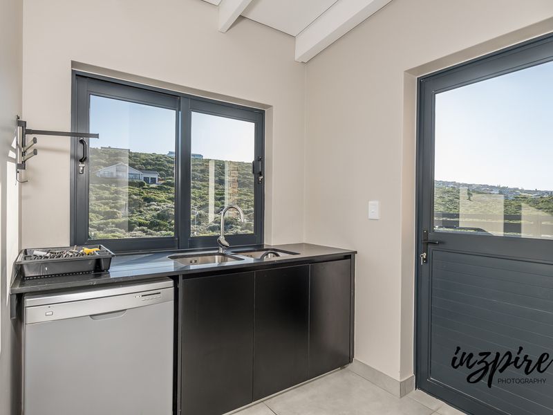 A clean and functional laundry area featuring dark cabinetry, a stainless steel sink, and direct access to the exterior through a stable door.
