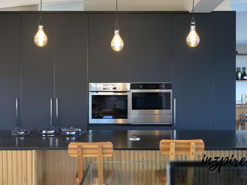Modern kitchen featuring dark matte cabinetry, a central island with a gas cooktop, and integrated stainless steel appliances.