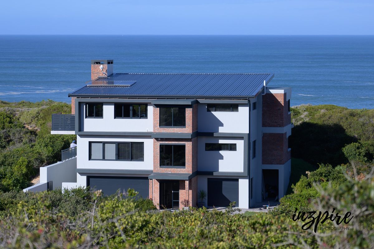 A modern multi-story coastal residence featuring a metal roof, brick accents, and expansive ocean views.