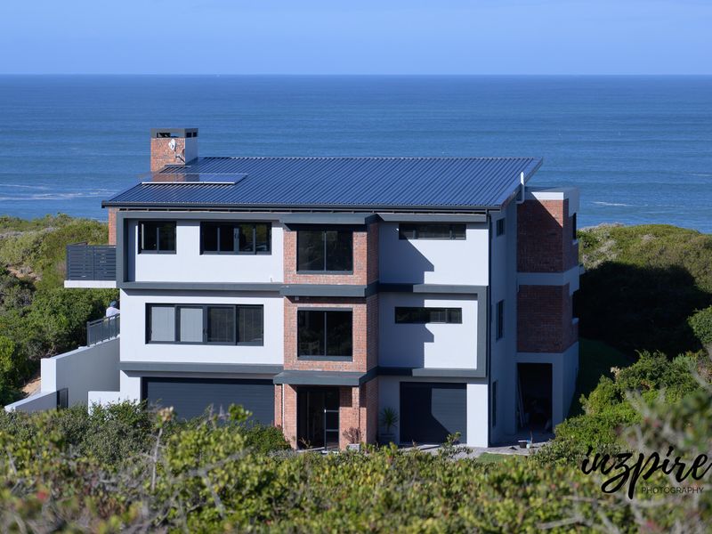 A modern multi-story coastal residence featuring a metal roof, brick accents, and expansive ocean views.