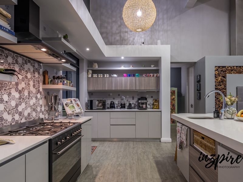 Modern kitchen featuring a gas stove, extractor fan, stone-topped island with sink, and stylish hexagonal tiled splashback with ample built-in cabinetry.