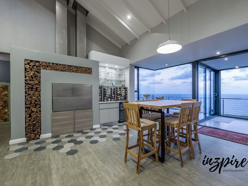 Modern open-plan living area featuring a built-in braai, integrated wine storage, vaulted ceilings, and expansive sliding doors opening to an ocean view.