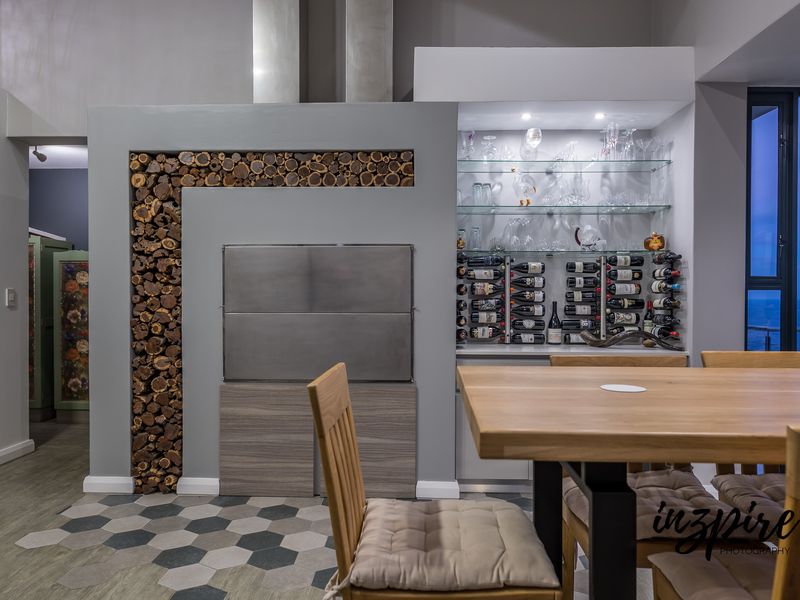 Modern living area featuring a built-in stainless steel braai, decorative wood storage, and a custom illuminated wine display with glass shelving.