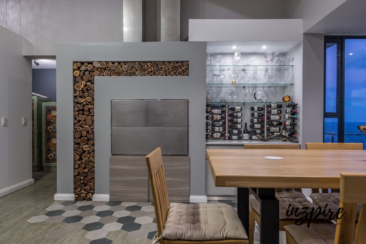 Modern living area featuring a built-in stainless steel braai, decorative wood storage, and a custom illuminated wine display with glass shelving.