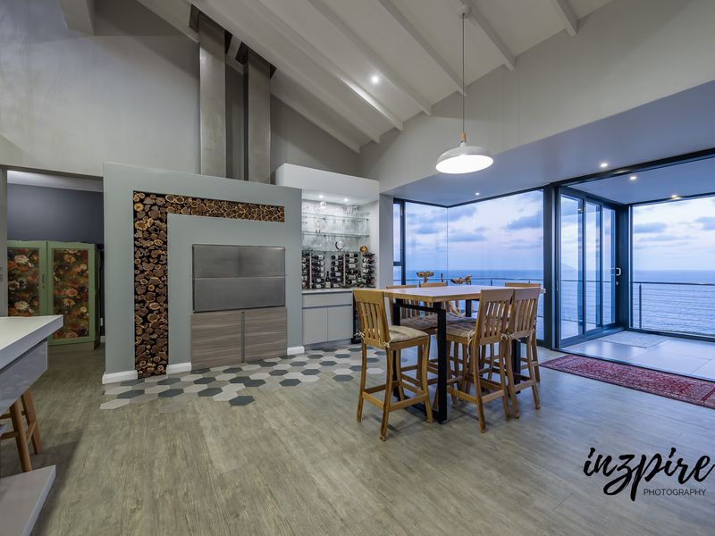 Modern open-plan living area featuring a built-in braai, wine storage, and expansive sliding glass doors opening to a scenic ocean view.