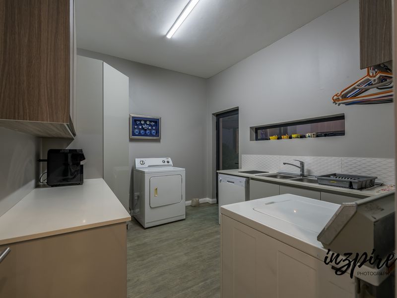 A functional laundry room featuring built-in cabinetry, a double sink with mixer tap, tiled splashback, and durable vinyl flooring.