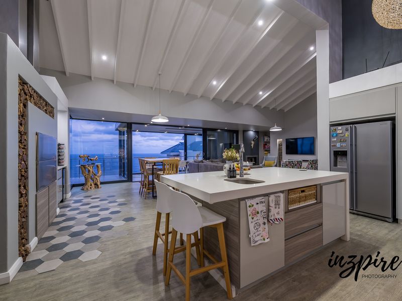Spacious open-plan living area featuring a modern kitchen island, vaulted ceilings, and large sliding doors opening to a scenic ocean view.