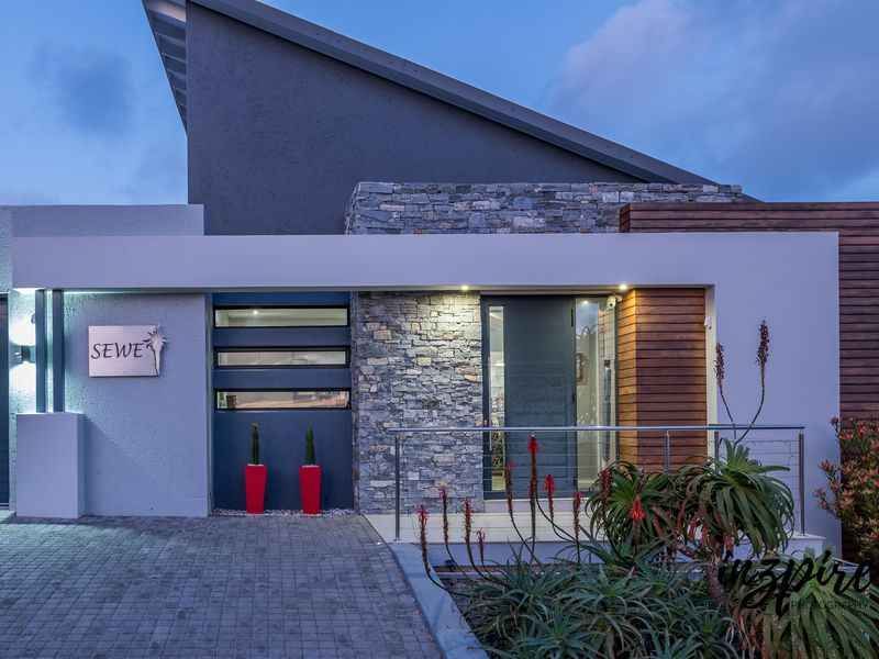 Modern front facade featuring a combination of stone cladding, timber accents, and a paved driveway with integrated exterior lighting.