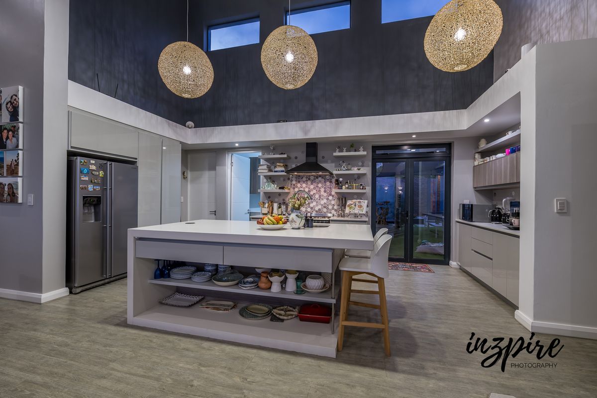 Modern open-plan kitchen featuring a large central island, high ceilings with clerestory windows, sleek cabinetry, and direct access to the outdoor area.
