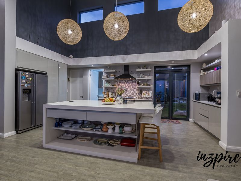 Modern open-plan kitchen featuring a large central island, high ceilings with clerestory windows, sleek cabinetry, and direct access to the outdoor area.