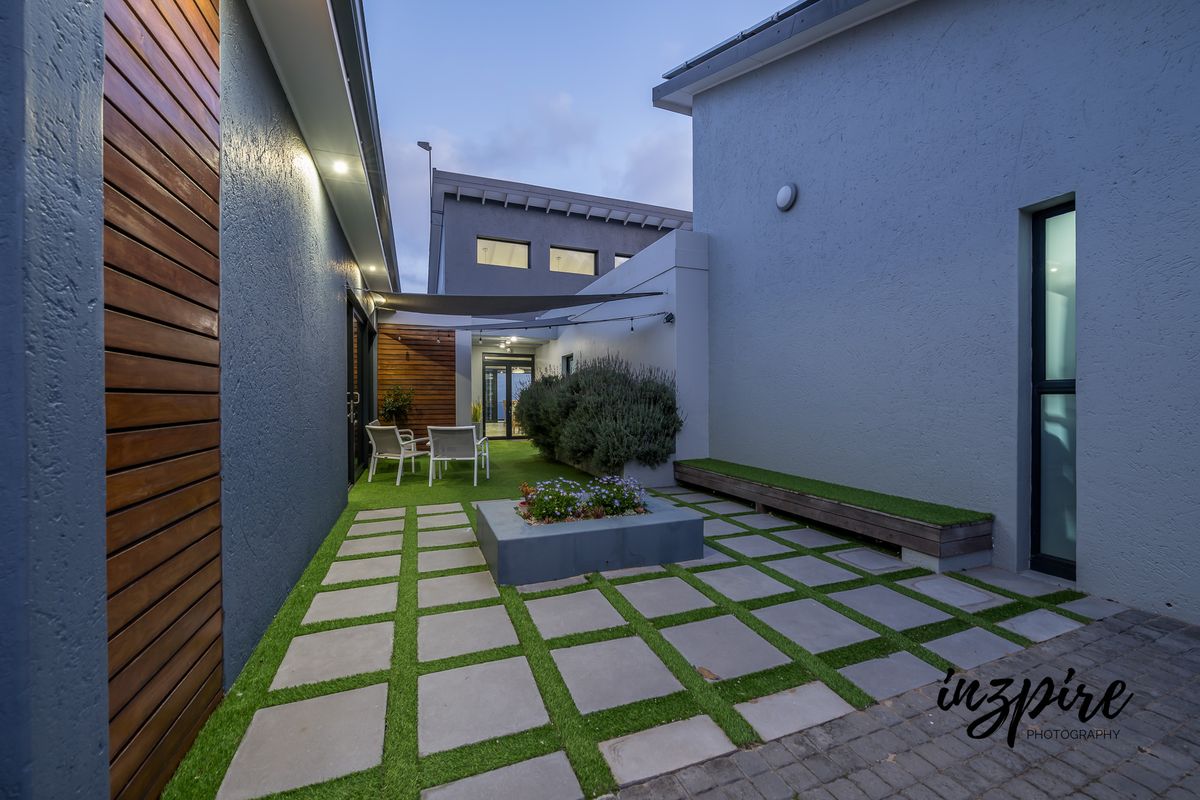 A modern, well-maintained rear courtyard featuring a paved patio with artificial turf, a built-in planter box, and a built-in bench.
