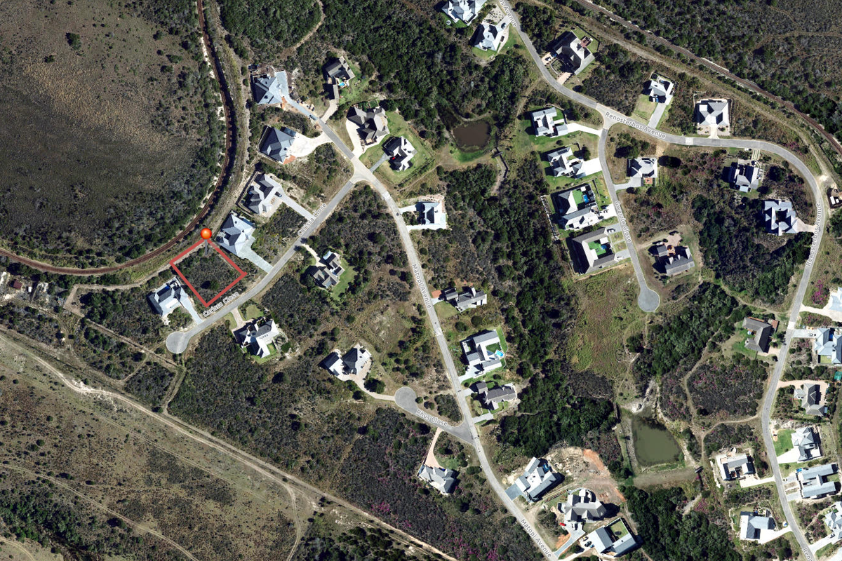 Aerial view of a vacant residential plot highlighted in red, situated within a developed estate with established road access and surrounding vegetation.
