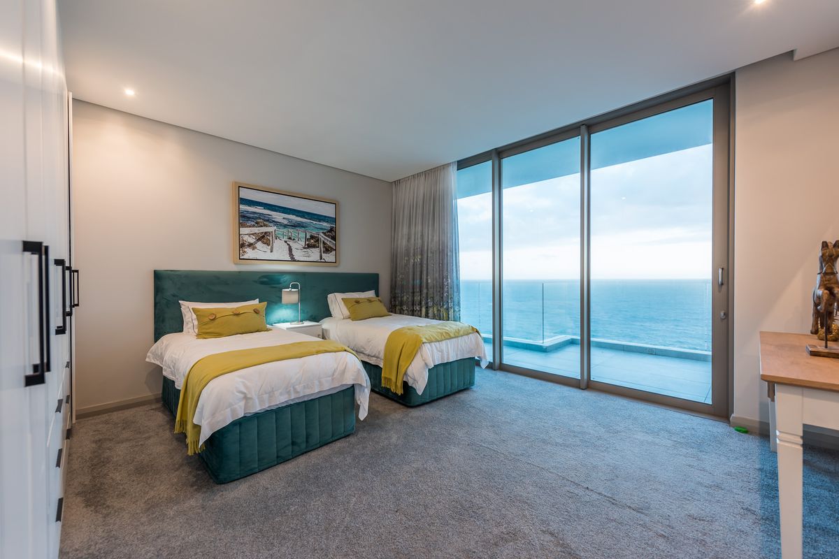 A modern bedroom featuring floor-to-ceiling sliding glass doors that open onto a balcony with expansive ocean views.