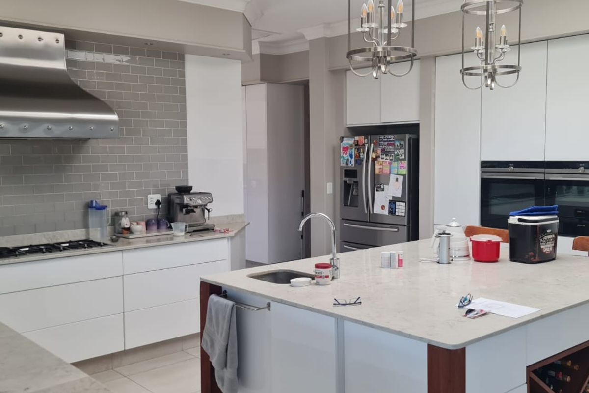 Modern kitchen featuring a large central island, stone countertops, subway tile backsplash, stainless steel extractor fan, and integrated double ovens.