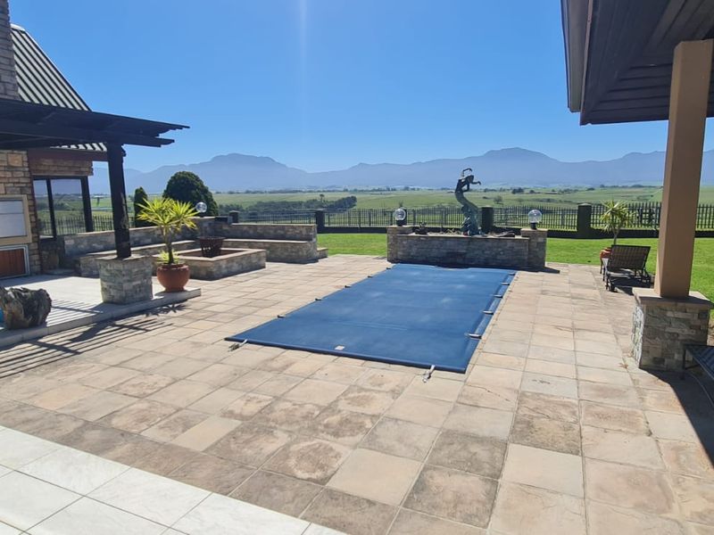 Spacious outdoor entertainment area featuring a swimming pool with cover, stone-paved patio, built-in braai, and panoramic mountain views.